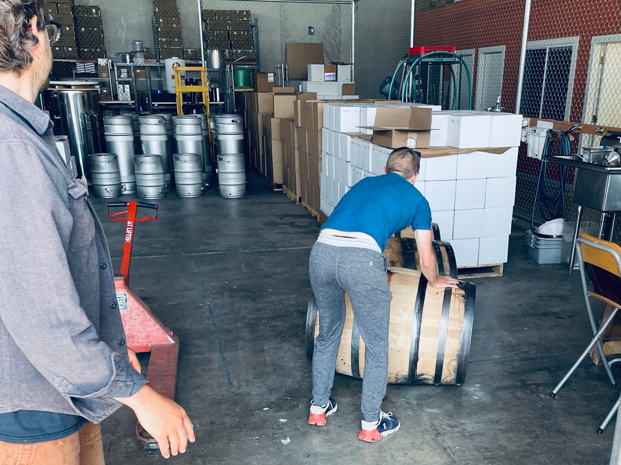 Two people rolling whiskey barrels into an industrial warehouse.