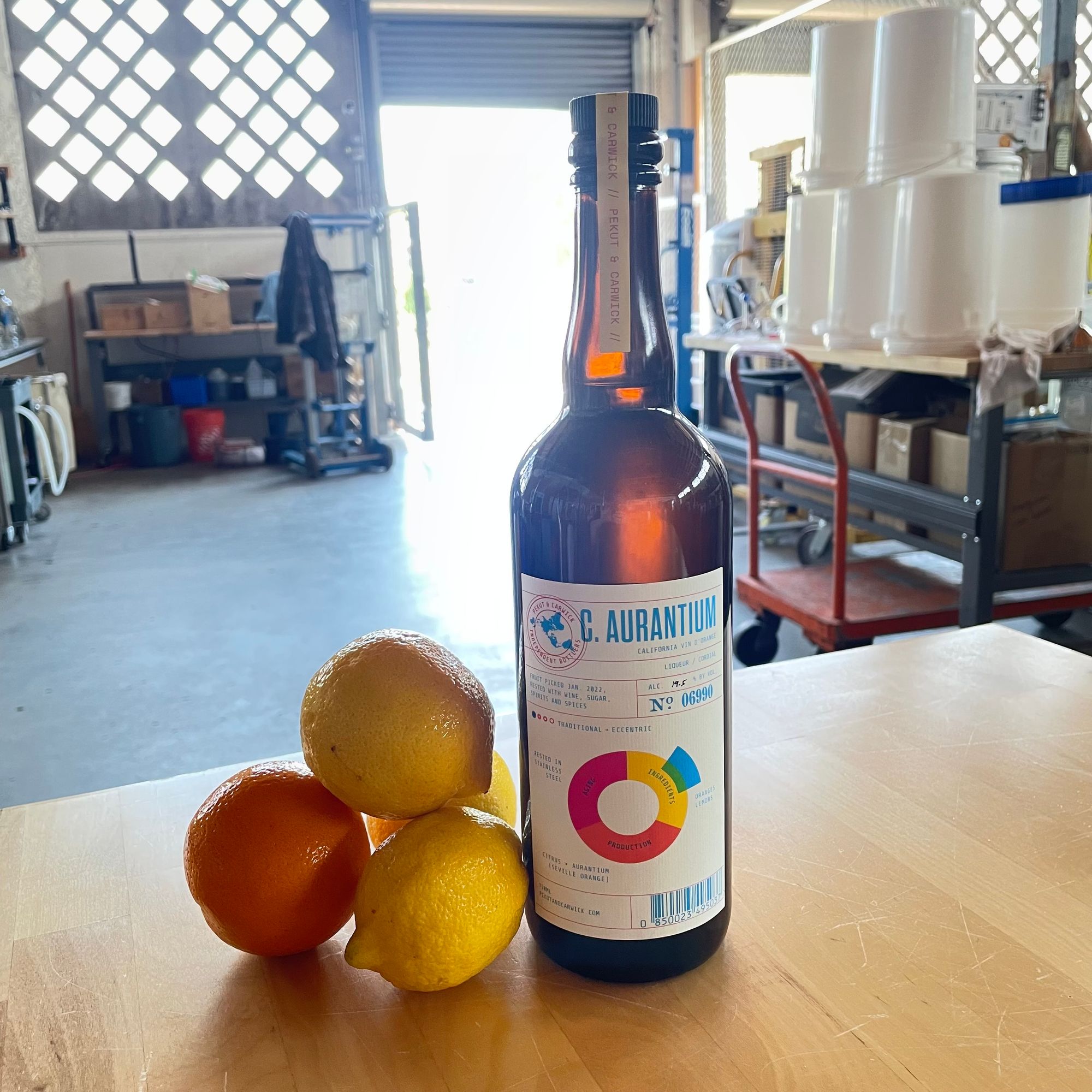 A bottle of Pekut & Carwick Vin d'Orange on a table next to fresh Seville oranges and lemons.