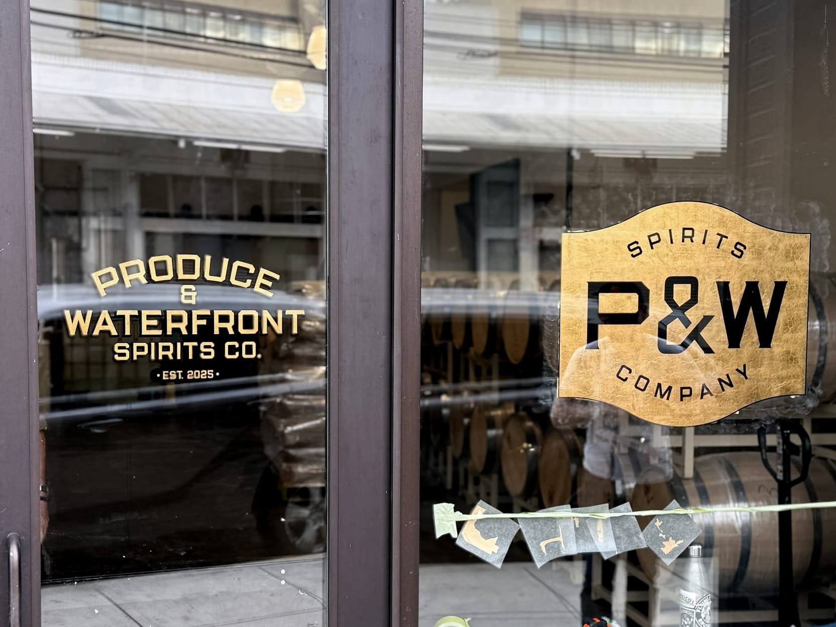 The P&W Spirits Company glass front doors, with signage reading "Produce and Waterfront Spirits Co. EST 2025".