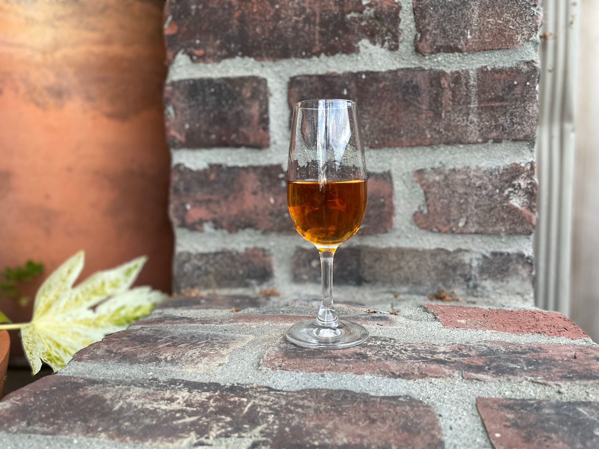 A copita glass of amber colored whiskey sits on a brick ledge. 