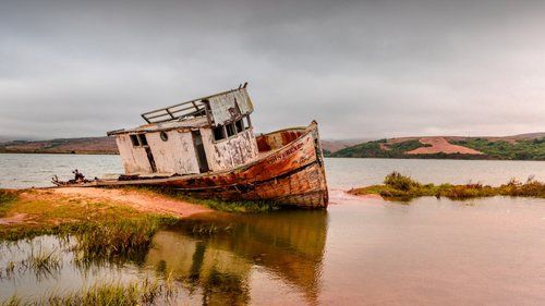 An old ramshackle boat is grounded in low waters and lit by sunset light.