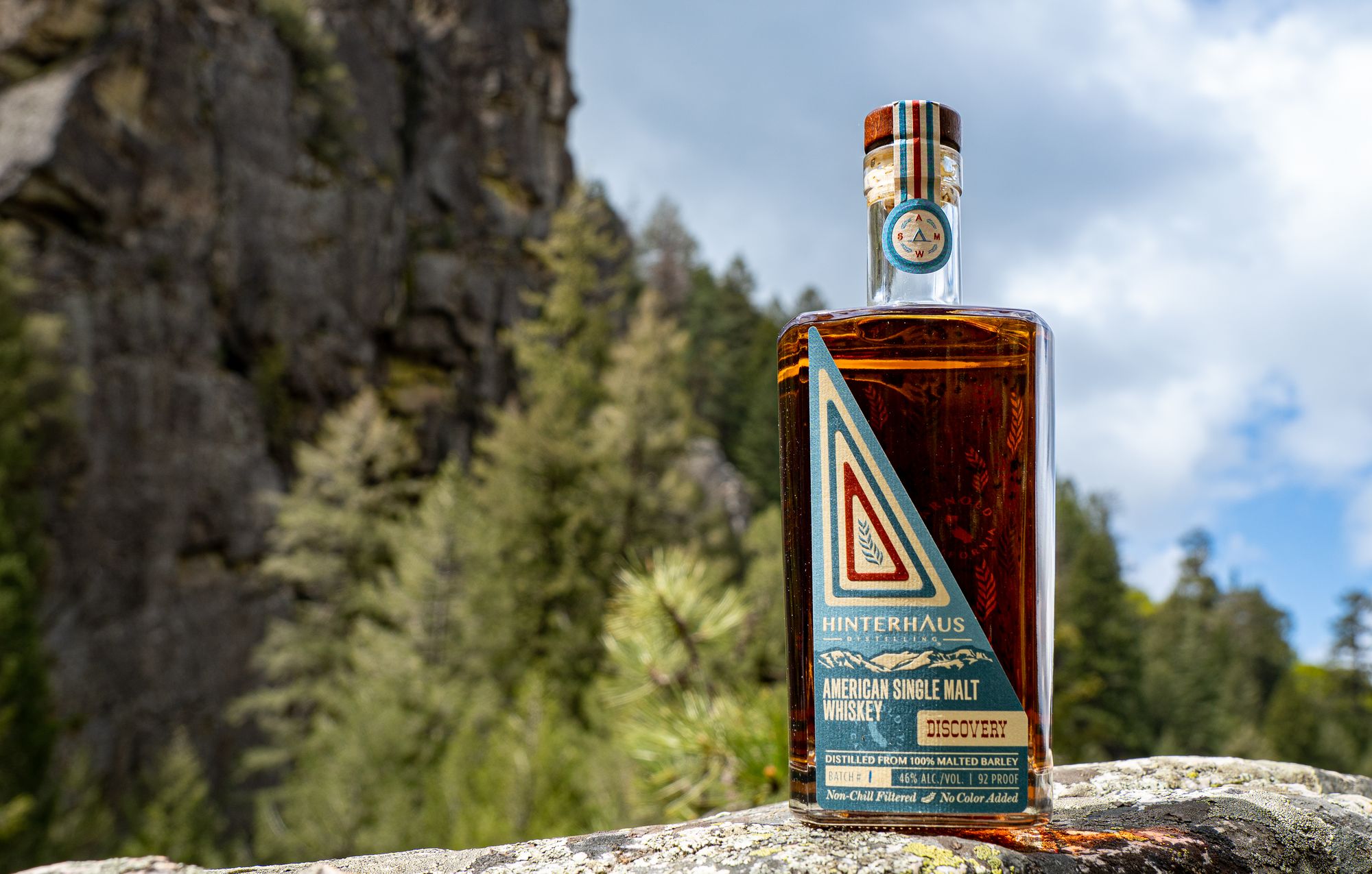 A bottle of Hinterhuas Distilling American Single Malt Whiskey sits atop a boulder in the Sierra 