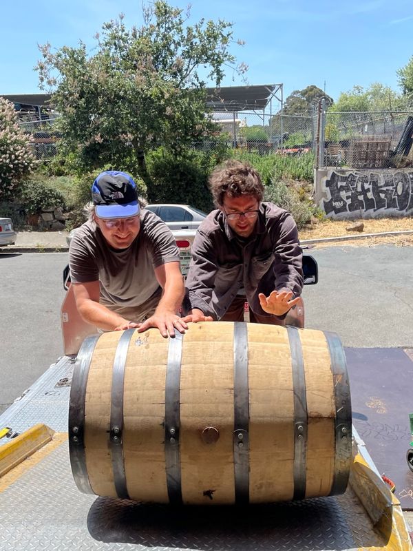 Two men rolling a whiskey barrel up a ramp.