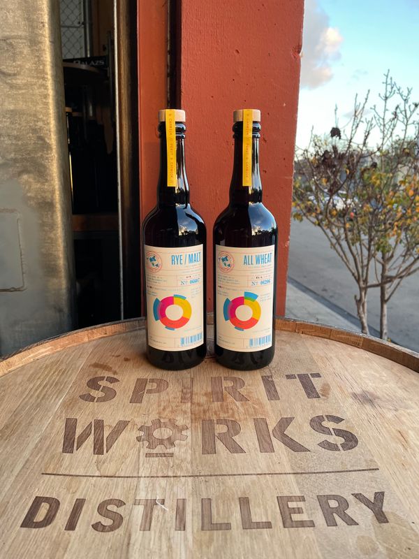 Two bottles of Pekut and Carwick whiskey on a branded barrel.