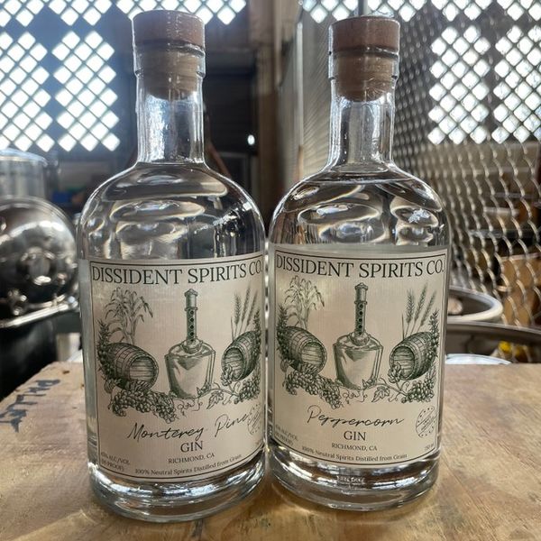A bottle each of Monterey Pine Gin and Peppercorn Gin sit on a wooden table.