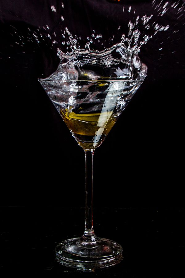 A martini splashes high above its glass against a dark background.